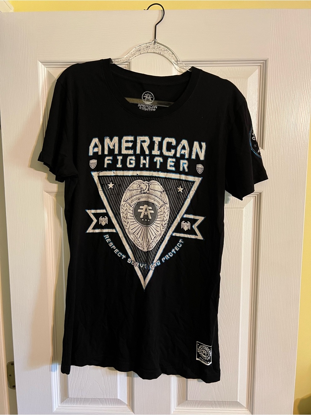Women’s American Fighter Black Tee with White and Blue Badge Graphic